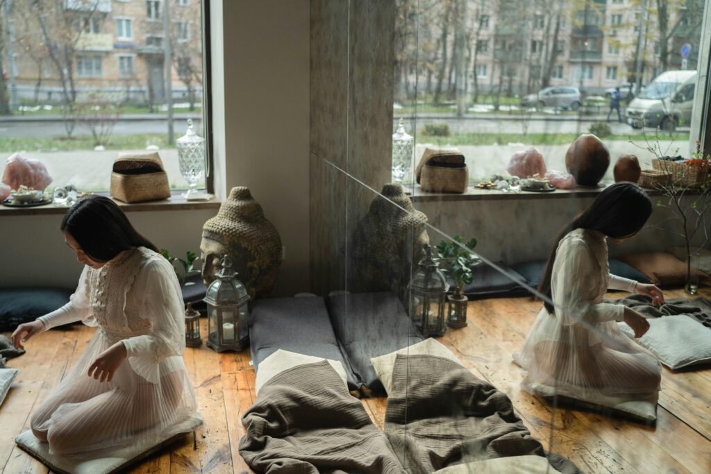 A woman meditates in a tranquil, sunlit room adorned with crystals and plants. Reflection adds depth.