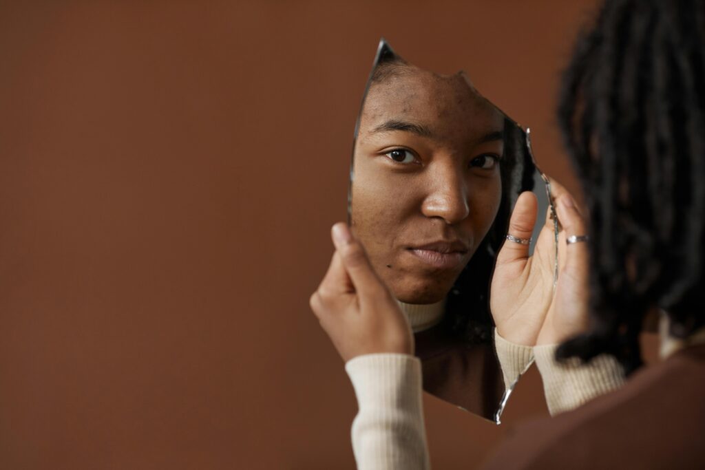 A woman holding and looking into a broken mirror, reflecting on self image and identity.