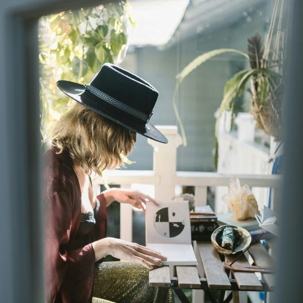 A woman in a hat reading tarot cards on a sunlit balcony surrounded by crystals.