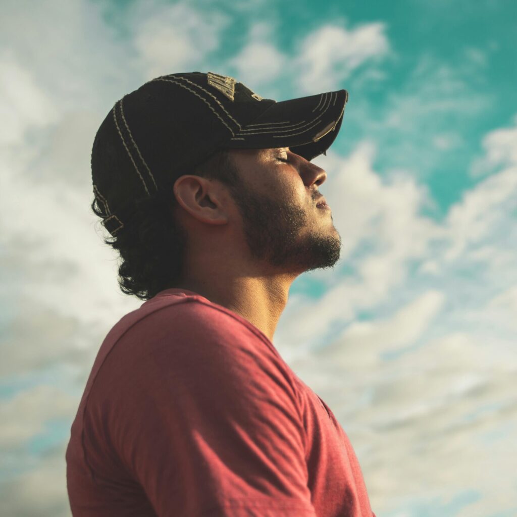 A man enjoys outdoor relaxation and mindfulness beneath a bright, cloudy sky, exuding calm and peace.