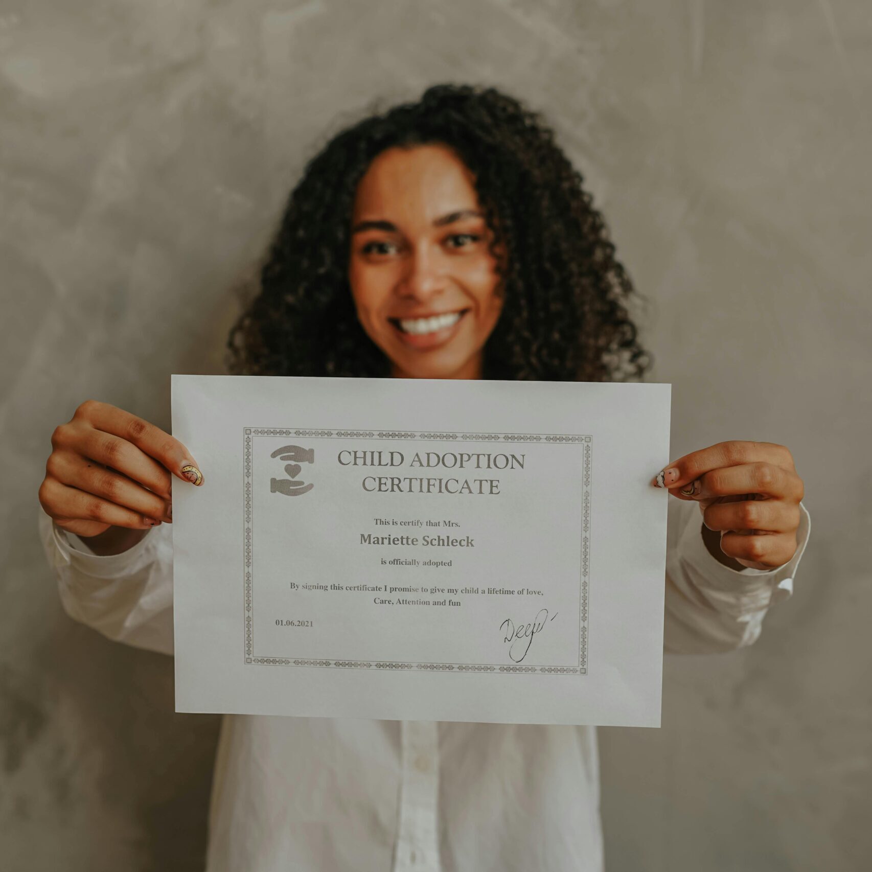 A smiling woman proudly holds a child adoption certificate indoors.